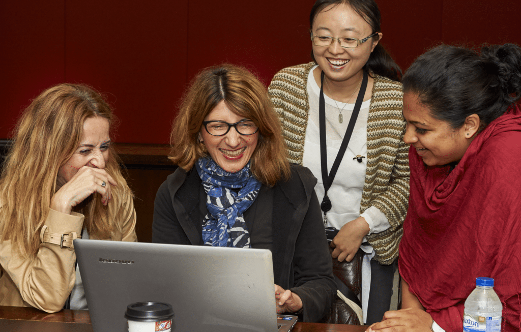 A group of four people laughing while sitting around a laptop.