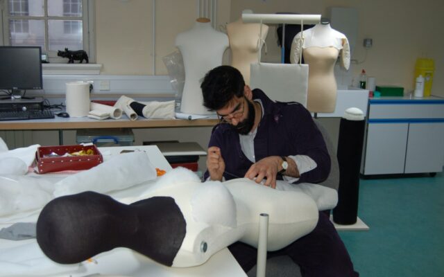 A man in a studio working with textiles and mannequins