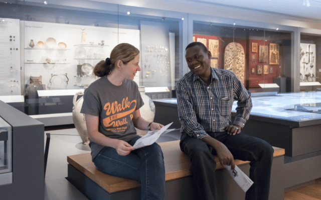 Two people sit in a museum gallery holding museum guides.