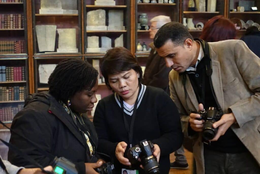 Three people holding cameras gather around to look a photograph taken by the person in the middle.