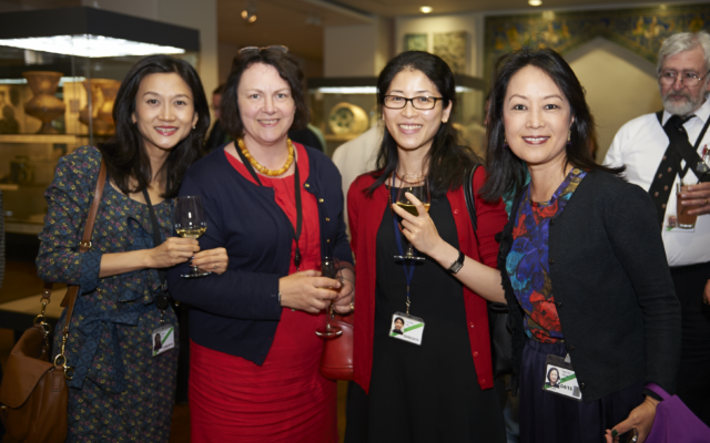 Four people smiling in a line smile for a photograph at a drinks reception