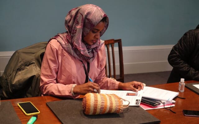 A woman in pink clothes and head scarf sits examining a museum object