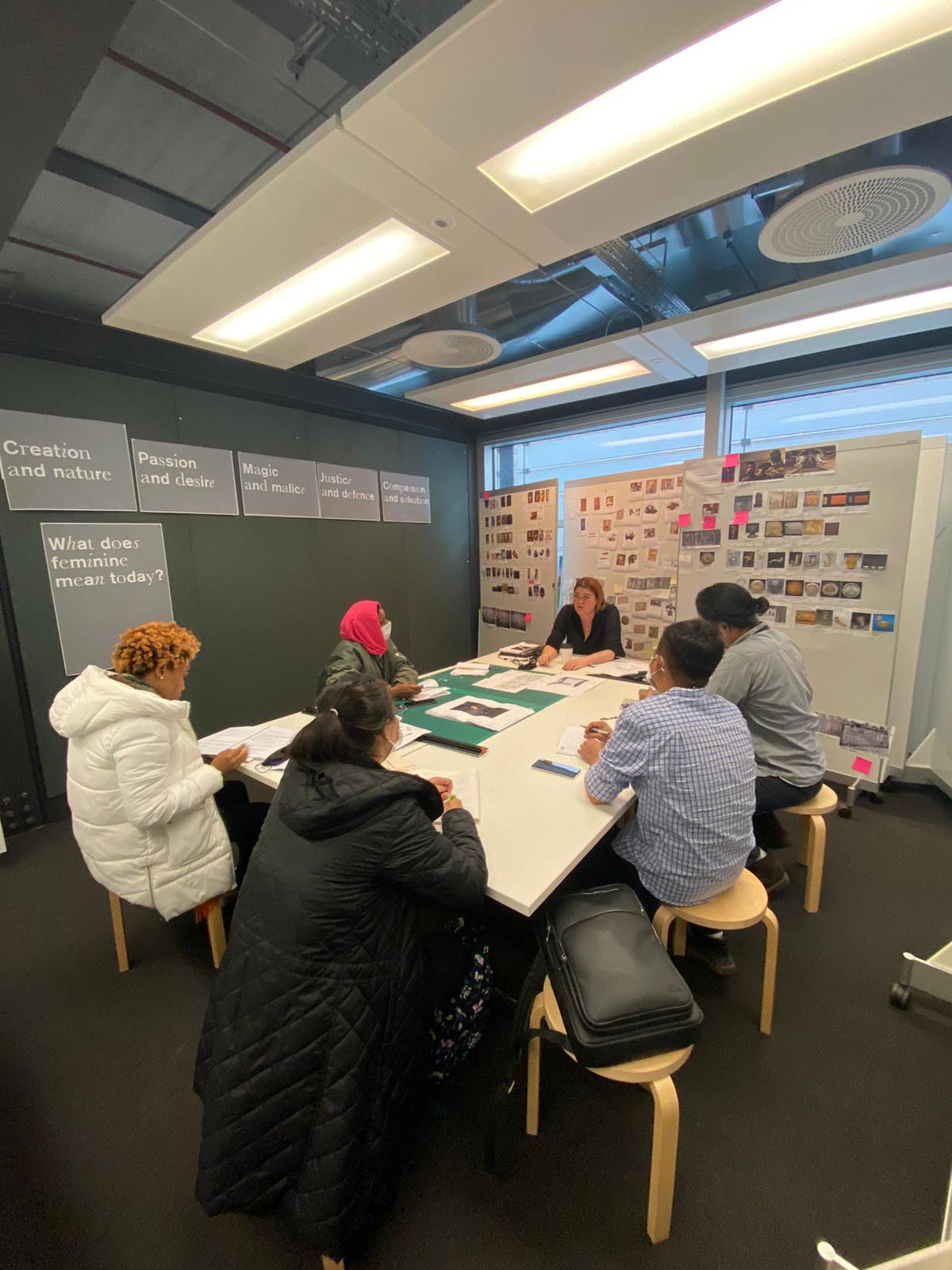 Six people sit around a table surrounded by whiteboards covered in notes and images