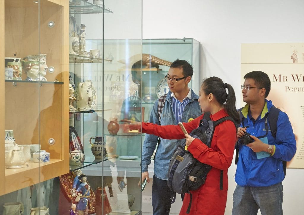 Three people look at a museum display place. A person wearing a read coat points at the case.