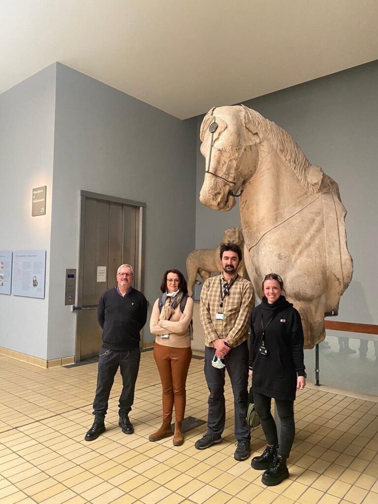 Four people stand in front of a stone statue depicting a horse.