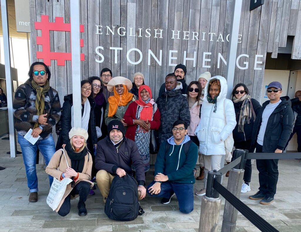 A group of people stand for a photo in front of a sign for Stonehenge