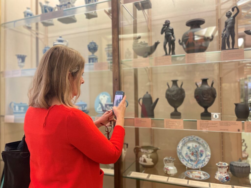 Eneida de Lemos, wearing an orange top, takes a photo of a museum display 
