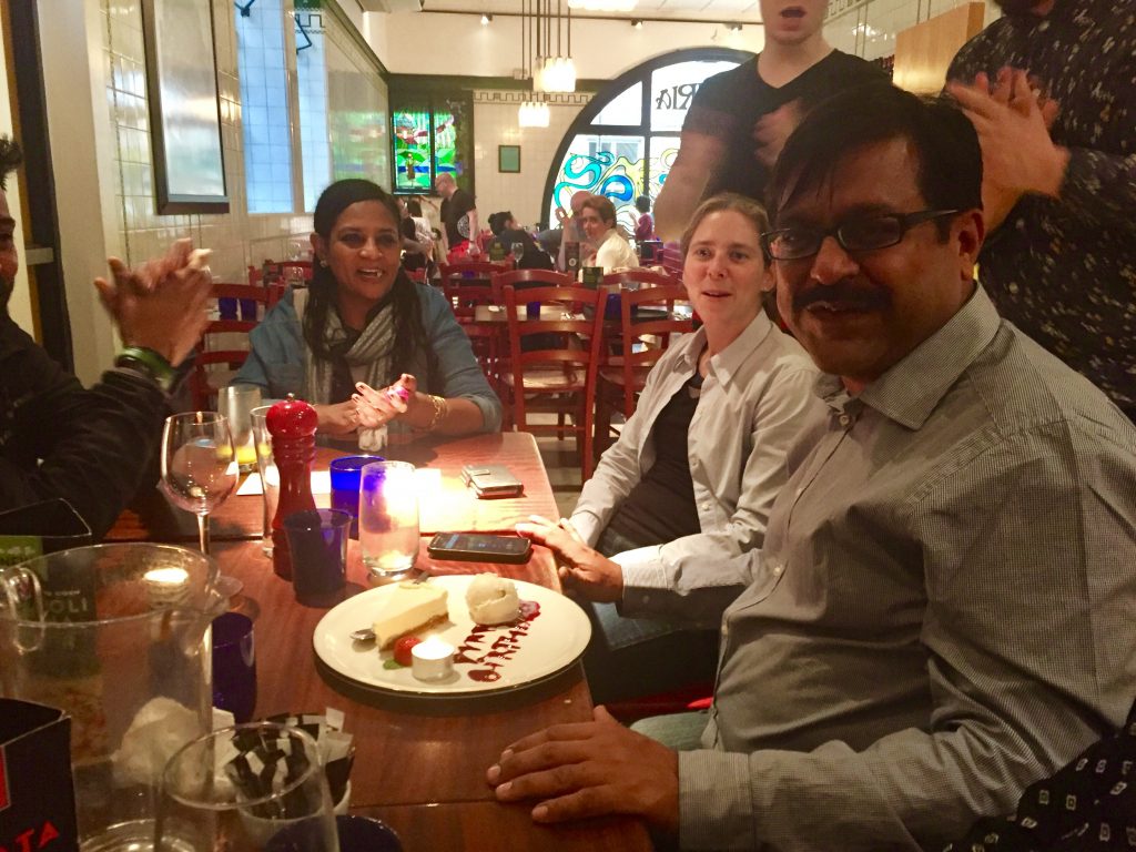 Mahesh celebrates his birthday with a cake with candles, sitting around ITP colleagues in a restaurant