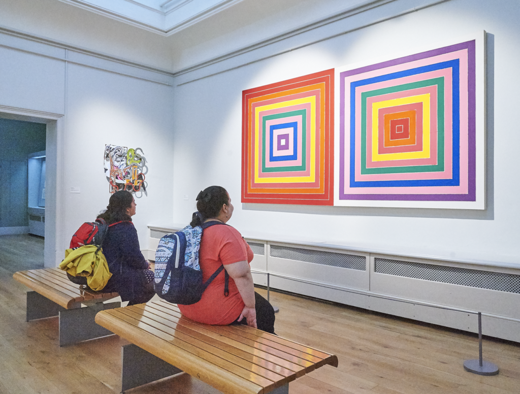 Two people sit and look at an art work at Brighton Art Gallery