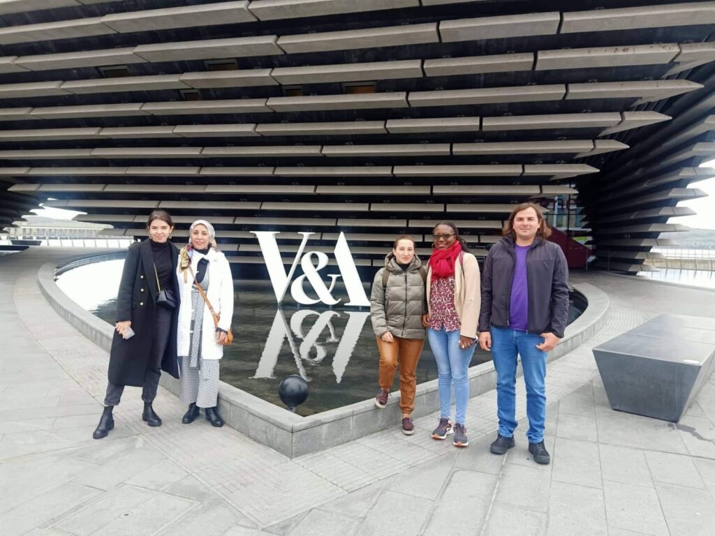 Five people stand in front of a sign for the V&A Dundee