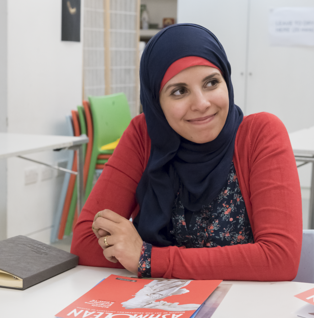 Heba Khairy sitting at a table, wearing a red top and navy headscarf