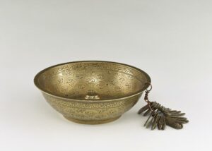 A brass bowl engraved with Arabic inscriptions and with engraved brass tags attached.