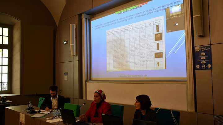Marwa giving her conference talk. She sits at a table between two colleagues with a presentation slide projected above them.