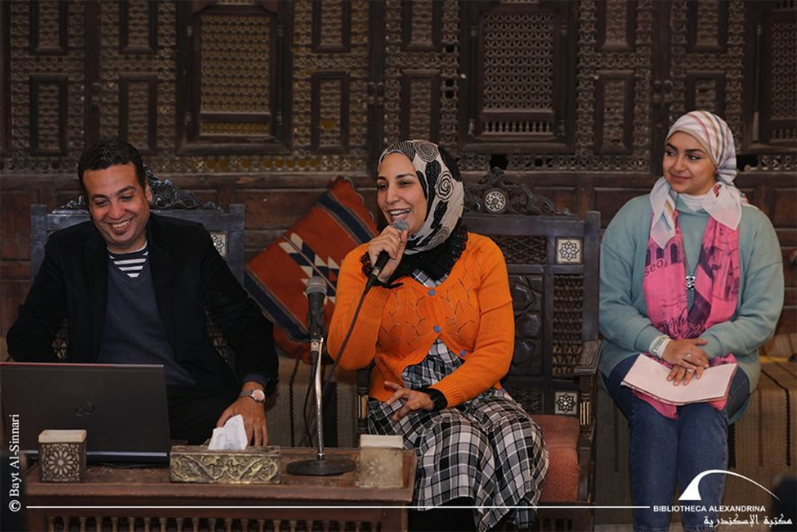 Nagwa chairs a seminar, holding a microphone and smiling.