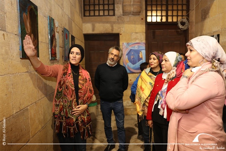 A group bring given a tour of the exhibition. Leader gestures towards a painting on a wall