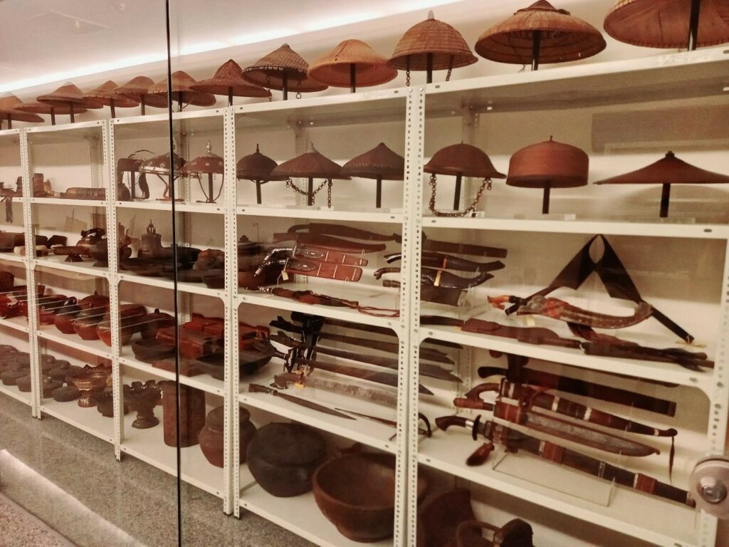 Shelves of objects at Ayala Museum, including hats, drinking vessels, swords and jewelry 