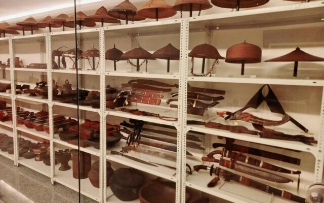 Shelves of objects at Ayala Museum, including hats, drinking vessels, swords and jewelry