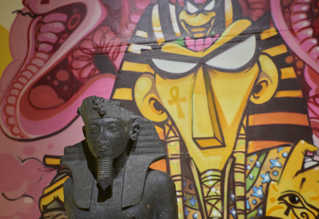 Close up of Tutankhamun reimagined display, with ancient statue of Tutankhamun placed in front of contemporary graffiti of Tutankhamun in the background.