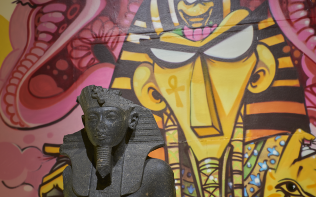 Close up of Tutankhamun reimagined display, with ancient statue of Tutankhamun placed in front of contemporary graffiti of Tutankhamun in the background.