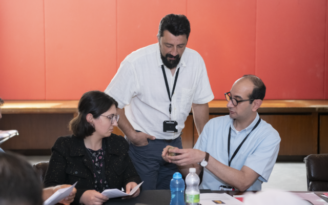 Senior Fellow Ciprian Dobra stands between two sitting ITP fellows doing an activity