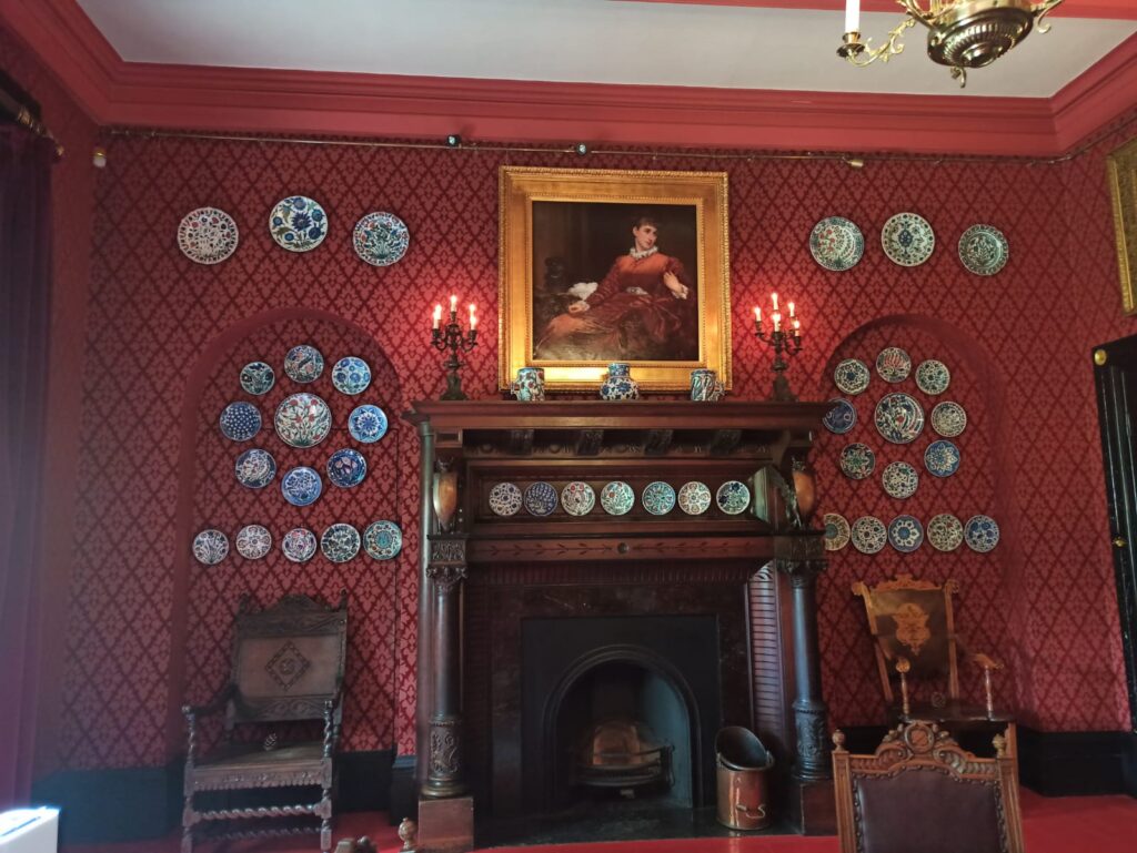 Fireplace in Leighton House. Walls are red with ceramic plates hanging 
