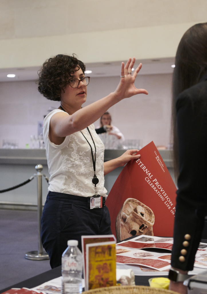 Catalina Cavelier stands holding a poster in her left hand. With her right hand she gestures to show how the poster should be placed on a wall.
