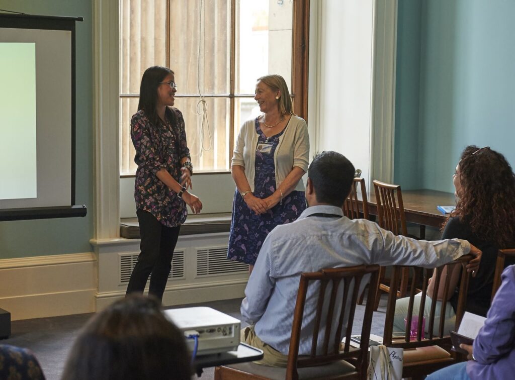 Yohana talking to a woman in front of a seated audience.