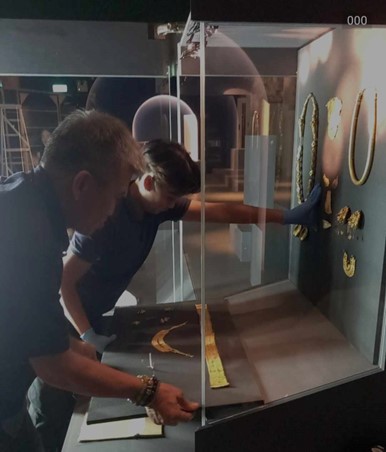 Photograph of two people moving objects into a glass case.