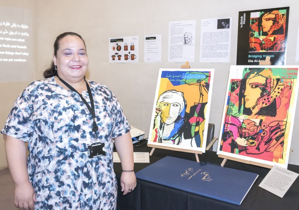 Mariem stood smiling next to a table and wall display with paintings.