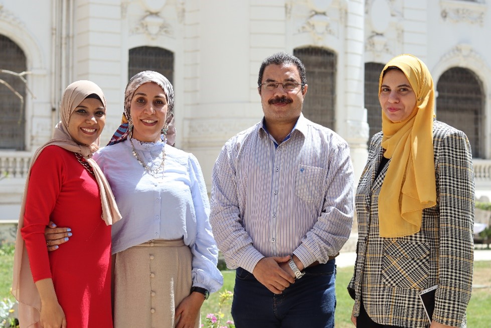 Photograph of three people - three women and one man - stood in a line and smiling.
