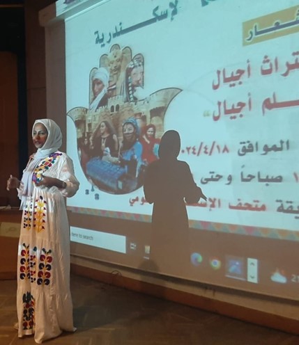 Photograph of a woman standing in front of a projected screen with Arabic text.