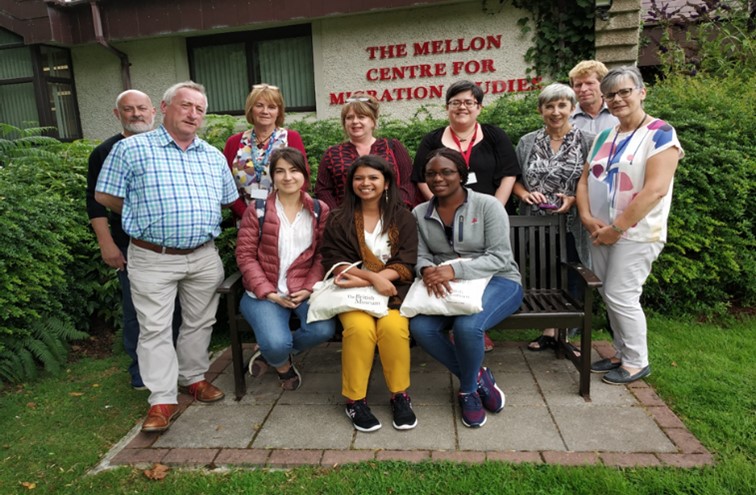 Photograph of a group of people sat on and around a bench.