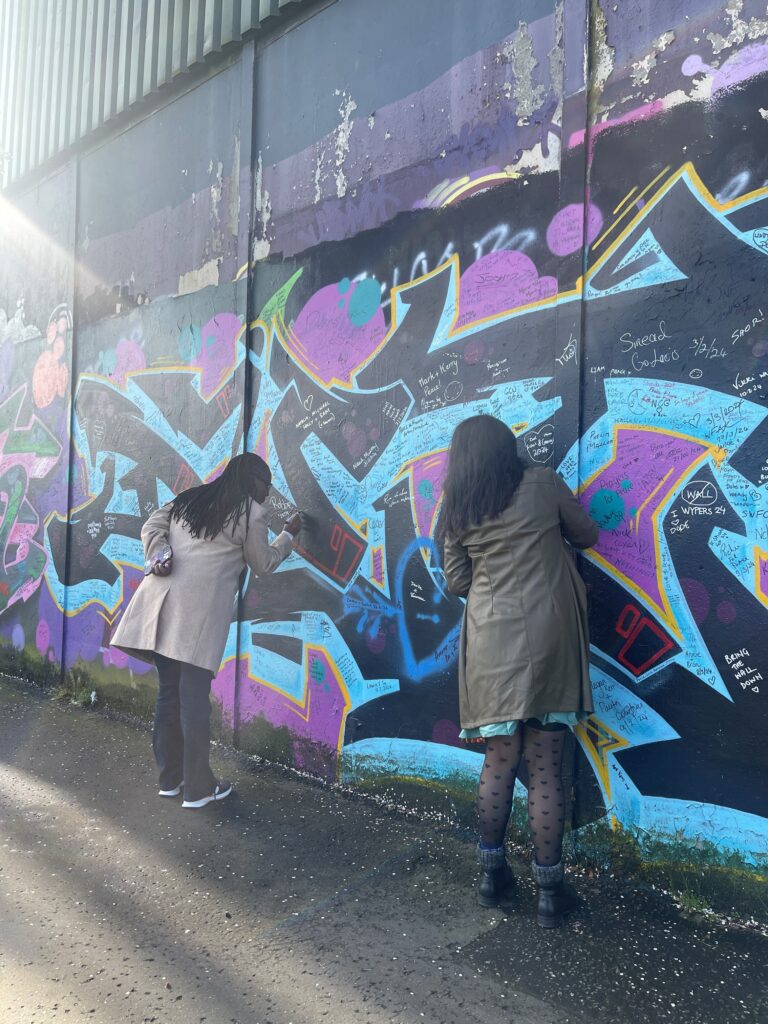 Photograph of two people writing on the Belfast Peace wall.