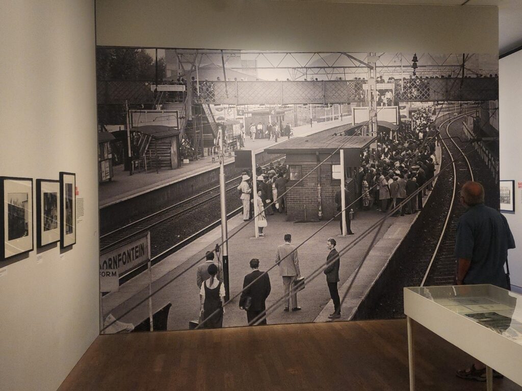 Photograph of a work by Ernest Cole, showing people waiting on a packed train platform.