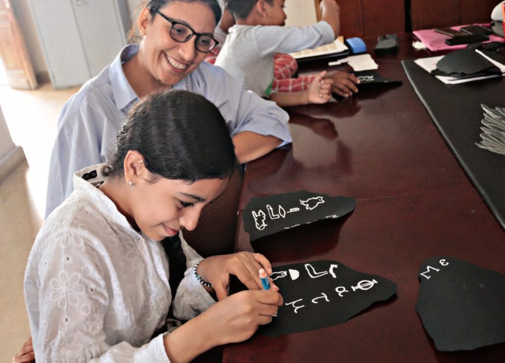 Photograph of a child drawing a replica of the Rosetta Stone, a woman is sat next to her, smiling.