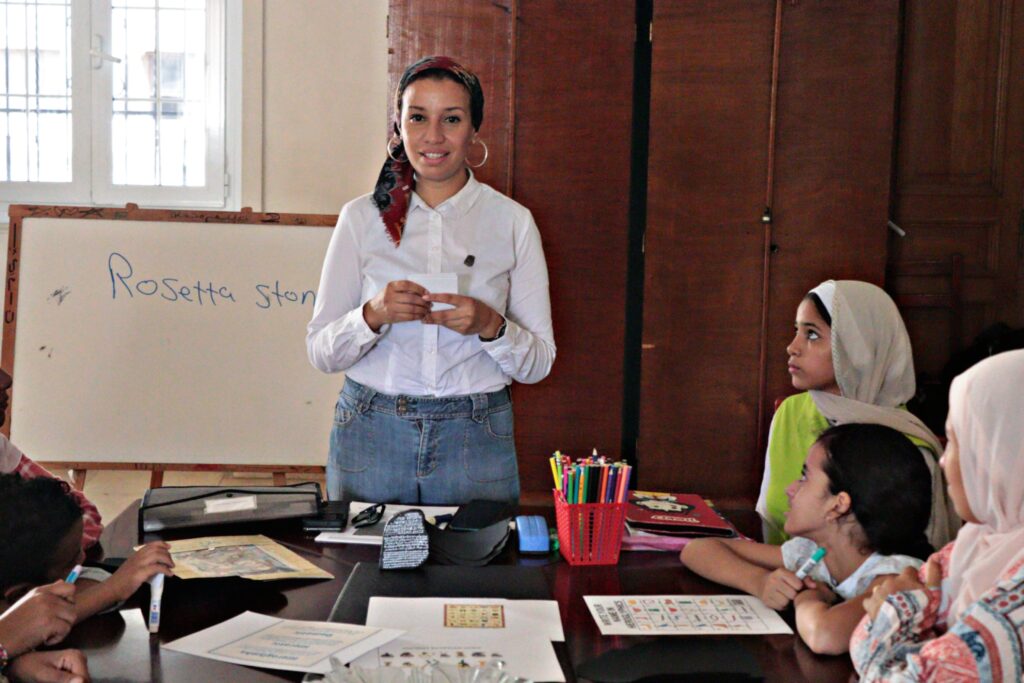 A woman stands in front of a table giving instructions.