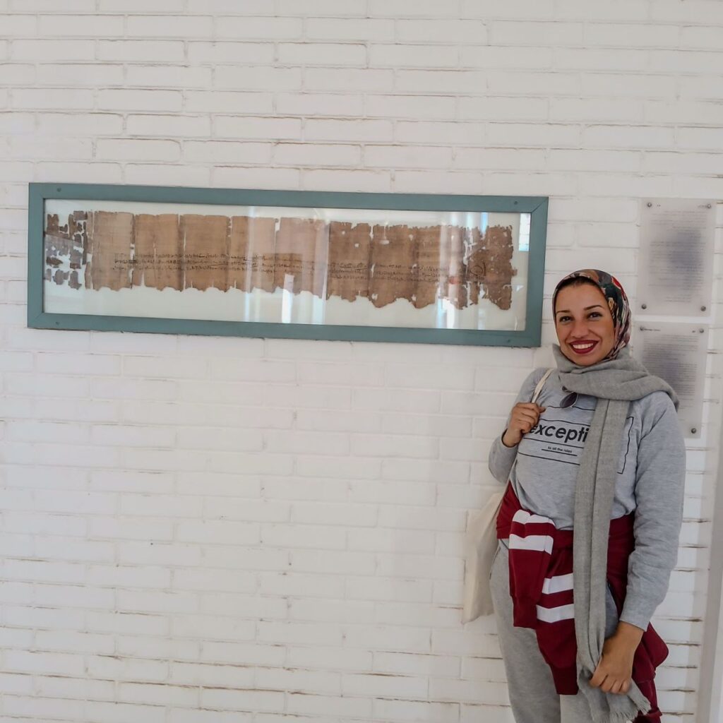 Photograph of a woman stood next to a framed papyrus